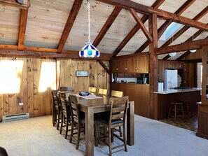 Un interior de fusta rústic amb taula de dinar, cadirees, llum penjant i zona de cuina.