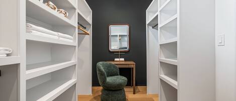Un vestidor con estantes blancos, una silla verde y un espejo sobre una mesa de madera.