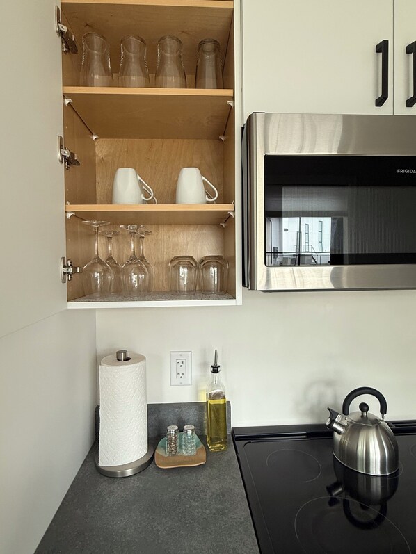 A kitchen with a built-in microwave, a kettle, a roll of paper towels, and a shelf with glassware.