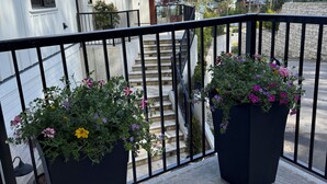 A balcony with two large flower pots, a staircase, and a white building in the background. - Hilltop Hideaway – Peaceful 2BR Suite, Near Beach Access and Mt. Baker Sunrises (North Saanich)