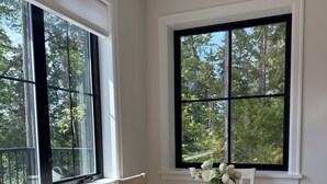 A dining area with a round table, white chairs, and a view of trees through large windows. - Hilltop Hideaway – Peaceful 2BR Suite, Near Beach Access and Mt. Baker Sunrises (North Saanich)