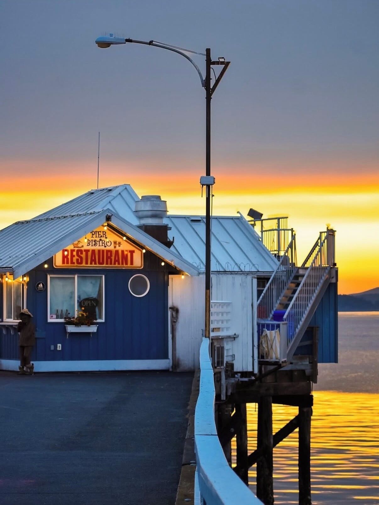 A pier with a restaurant named 'Pier Bistro' featuring a blue exterior, a staircase, and a view of the water.