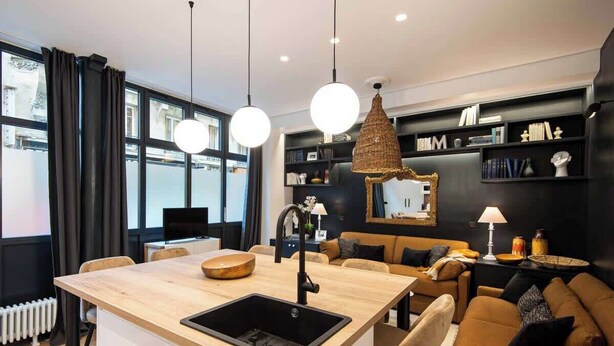 Una cocina moderna con una isla central, iluminación colgante y una zona de estar acogedora con un sofá y una mesa de centro.