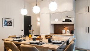 Una cocina moderna con armarios blancos, una mesa de comedor de madera e iluminación colgante.