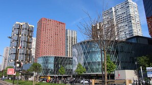 Un entorno urbano moderno con edificios altos, un edificio de paredes de vidrio y una calle arbolada.