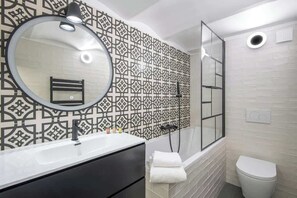 Un baño con un espejo redondo, una bañera, un inodoro y una cabina de ducha.
