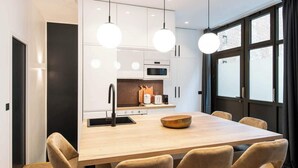 Una cocina moderna con armarios blancos, una mesa de comedor de madera y lámparas colgantes.