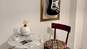 A room with a white wall, a framed black electric guitar, a wooden chair with a patterned cushion, a small round table with a marble top, a vintage-style telephone, and a decorative light fixture. - Soleja House, 1000 meters from Poetto beach and Molentargius Park (Quartu Sant'Elena)