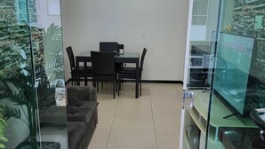 A modern living room with a glass partition, a dining area with a table and chairs, a sofa, and a television. - Setor Bueno, Academia Piscina Órion Business (Goiânia)