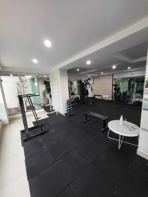 Ein Fitnessraum mit Trainingsgeräten, einer Bank und einem Tisch mit einer Wasserflasche.