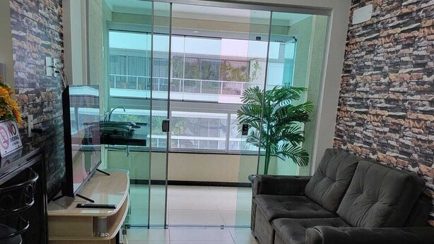 A living room with a sofa, a TV, a small table, and a plant. - Setor Bueno, Academia Piscina Órion Business (Goiânia)