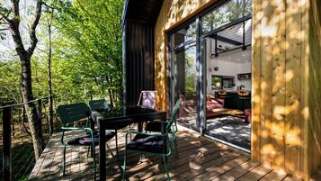 A wooden deck with a table and chairs, a glass door leading inside, and a view of the outdoors.