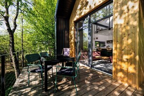 A wooden deck with a table and chairs, a glass door leading inside, and a view of the outdoors.