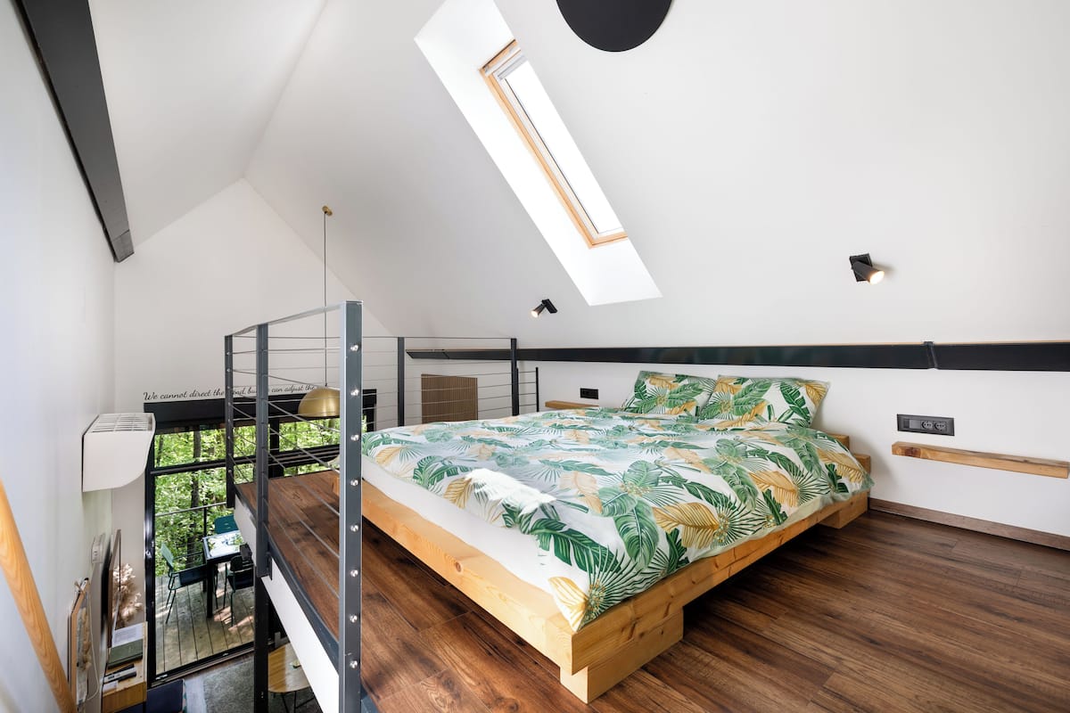 Une chambre à coucher avec un lit, une lucarne et une vue sur la verdure.