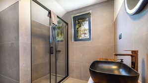 Ein modernes Badezimmer mit Duschabtrennung aus Glas, einem Holzwaschtisch und einem großen, schwarzen Waschbecken.