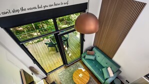 Ein modernes Wohnzimmer mit einem grünen Sofa, einem runden Couchtisch aus Holz und einem großen Fenster mit Blick auf eine Terrasse.