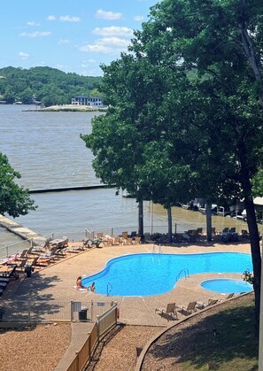 A swimming pool with lounge chairs, a wooden deck, and a view of a lake. - Lakefront Condo Balcony & Pool Near Margaritaville, Redheads Grill, Shorty Pants (Osage Beach)