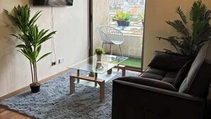 Una sala moderna con una mesa de centro de vidrio, un sofá, un televisor montado en la pared y un balcón con vistas a la ciudad.