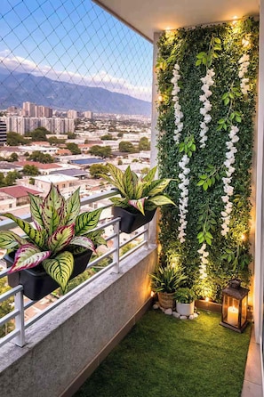 A balcony with a view of a cityscape, a green wall with white flowers, and potted plants. - Renovated and Spacious apartment in Santiago ! (Santiago)