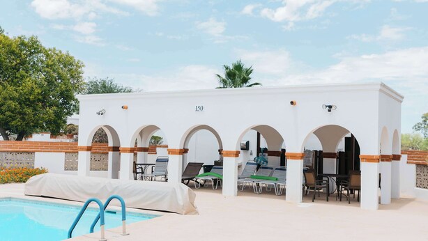 Uma área à beira da piscina com um espaço de estar coberto, espreguiçadeiras e piscina.