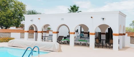 A poolside area with a covered seating area, lounge chairs, and a pool.