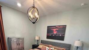 A bedroom with a large bed, two bedside tables with lamps, a ceiling light, a wardrobe, and a painting on the wall.