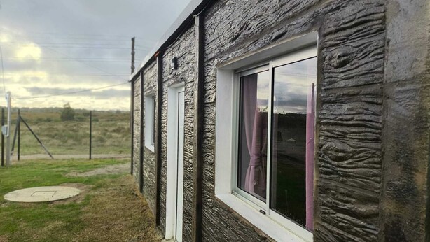 En bygning med en struktureret facade, et vindue med gardiner og et grønt område med en brønddæksel.