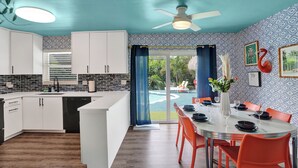 Una cocina moderna con armarios blancos, una isla central y una zona de comedor con sillas color naranja.