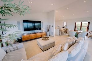 A spacious living area with a large flat-screen TV, a wooden console, a dining area, and a view of greenery. - Villa Tortuga - Oceanview House with Heated Pool (Culebra)