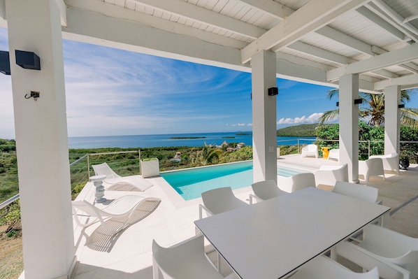 A covered outdoor area with a pool, white furniture, and a view of the ocean. - Villa Tortuga - Oceanview House with Heated Pool (Culebra)