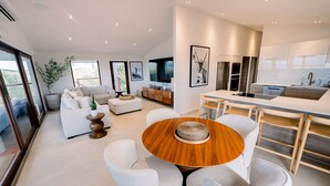 A modern kitchen with a central island, a dining area with a round table, and a living space with a sofa and a plant.
