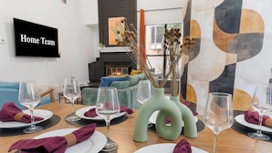 Een eetruimte met een tafel voor zes personen, een televisie aan de muur en een open haard op de achtergrond.