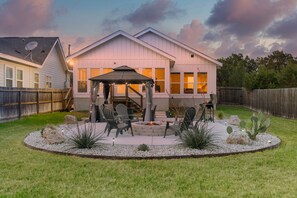 A residential backyard with a patio area, outdoor seating, and a fire pit.
