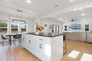 A spacious kitchen with white cabinetry, a central island, and a dining area with chairs.