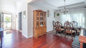 A spacious living room with hardwood flooring, a wooden cabinet, a dining table with chairs, and a piano. - 4BR/3BA, 3700 SqFt, Luxury Home in Durham near RDU, Duke, and UNC (Durham)