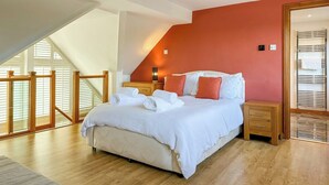 Une chambre à coucher avec un lit, des tables de chevet en bois, un mur d’accent rouge, une lucarne et un escalier en bois.