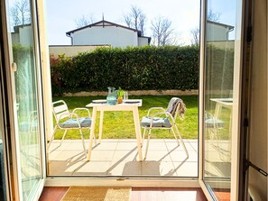 A patio with a table and chairs, a glass door, and a view of a hedge and house in the background. - Maritime garden apartment with terrace only 300m from the beach / WLAN + parking space (Kühlungsborn)