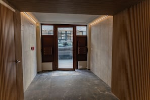 A hallway with a door leading to a parking area, a fire alarm, and a wall with vertical lines. - OneLuxStay Antwerp Near Central Station (Antwerp)