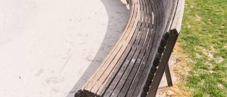 A curved wooden bench in a park with trees and a building in the background.