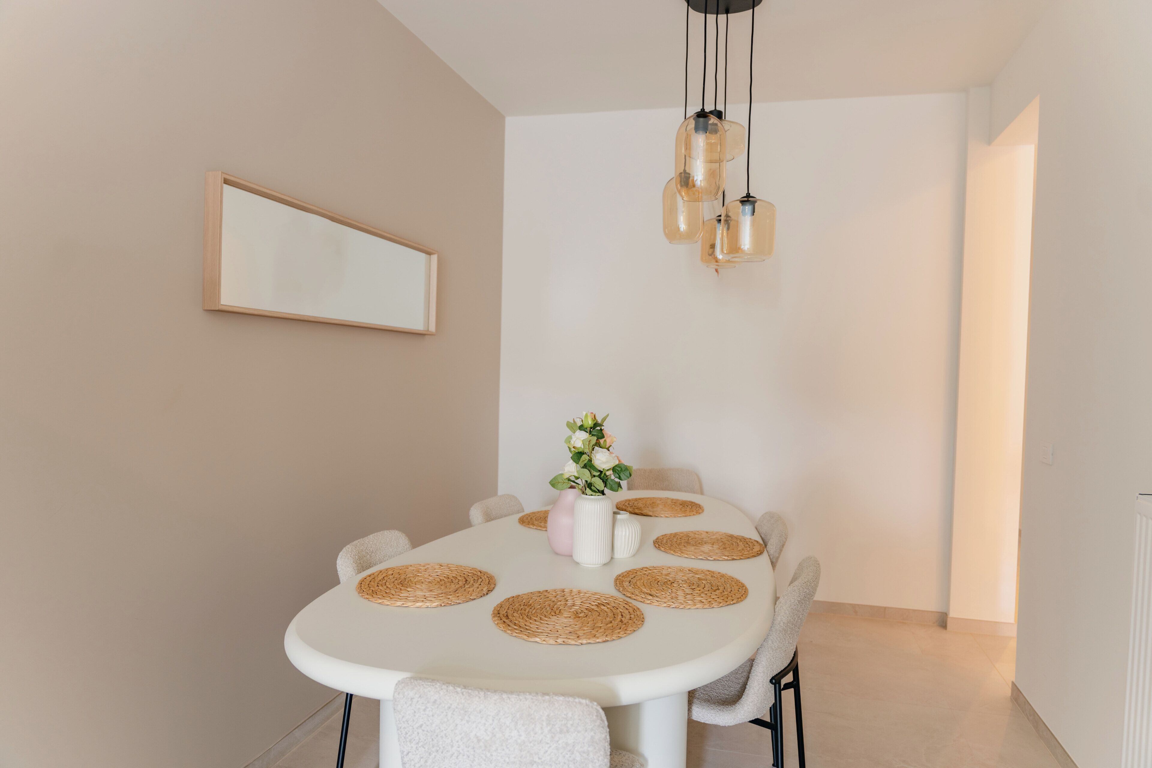 Een eetgedeelte met een ronde tafel, stoelen, een vaas met bloemen en een hanglamp.