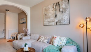 A living room with a sectional sofa, a painting, a floor lamp, and a radiator. - OneLuxStay Antwerp Near Central Station (Antwerp)