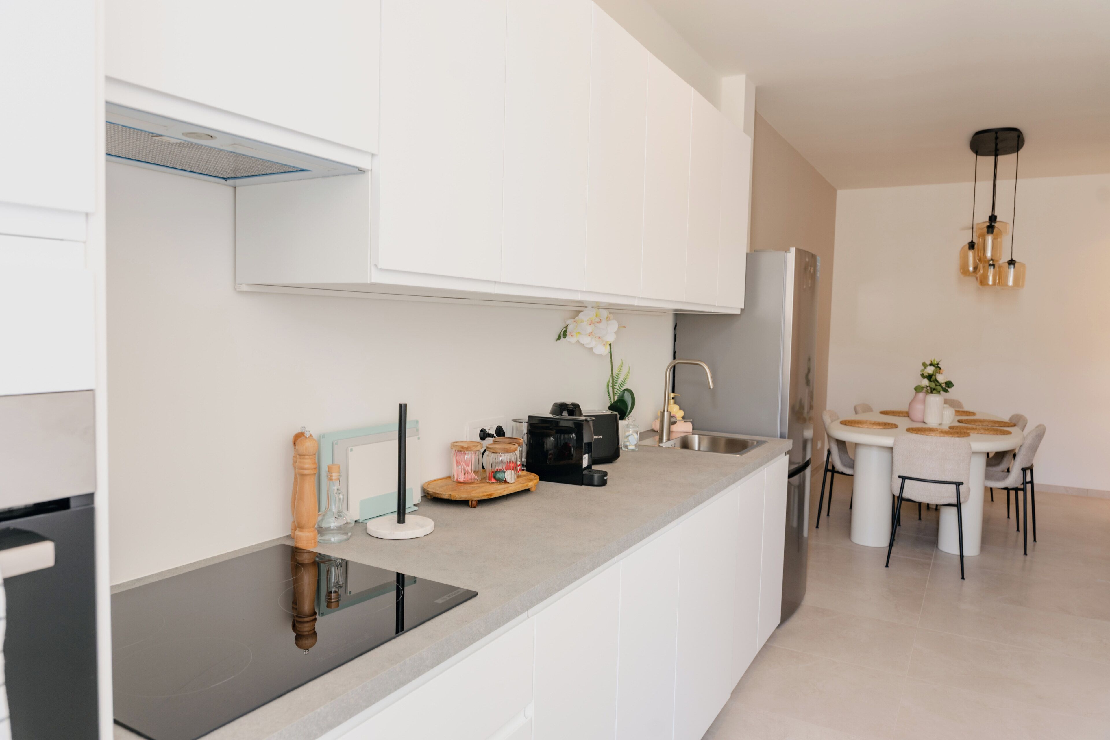 A modern kitchen with a central island, white cabinetry, and a dining area with a round table and chairs.