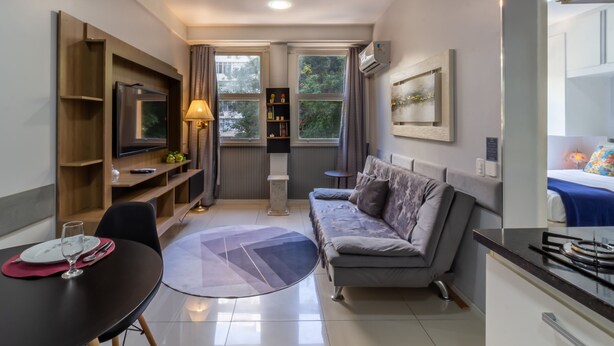 Uma sala de estar moderna com sofá, TV, mesa de jantar e vista para o verde lá fora.