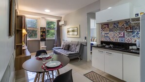 Cozinha compacta com área de refeições, sofá e janela com cortinas.