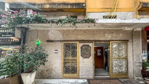Entrada de um edifício com fachada de pedra, um vaso grande com planta e uma placa indicando consultório médico.