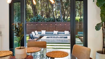 Un intérieur moderne avec une table à manger en verre, des chaises, un canapé et un foyer extérieur.