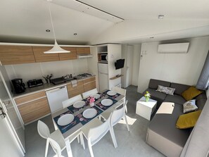 A modern kitchen with white cabinets, a dining table set for four, and a grey sofa with cushions. - 6-person mobile home rental with large water park (Carnac)