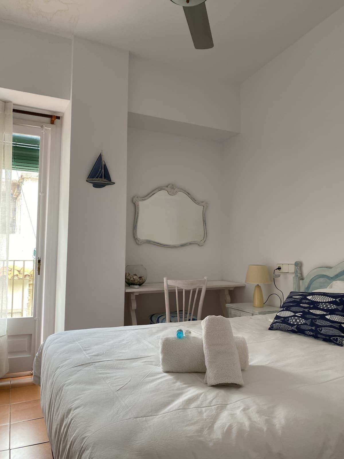 A bedroom with a bed, a chair, a desk, a mirror, and a ceiling fan.