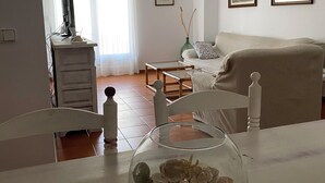 A living room with a television, a glass bowl on a table, a ceiling fan, and two framed pictures on the wall. - Spacious apartment with ocean view, 2 steps from the beach, ideal for families! (L'Escala)
