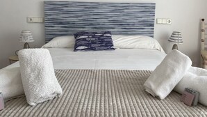 A neatly made bed with a striped headboard, two pillows, two white towels, and a striped rug. - Spacious apartment with ocean view, 2 steps from the beach, ideal for families! (L'Escala)